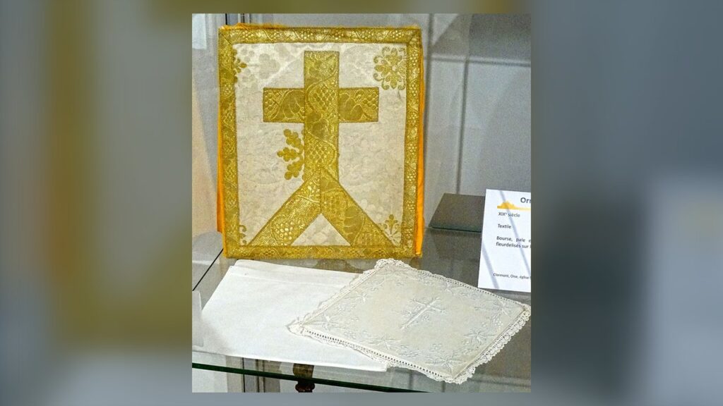 Bolsa bordada com cruz dourada, pala e corporal de linho branco, alfaias que acompanham o cálice