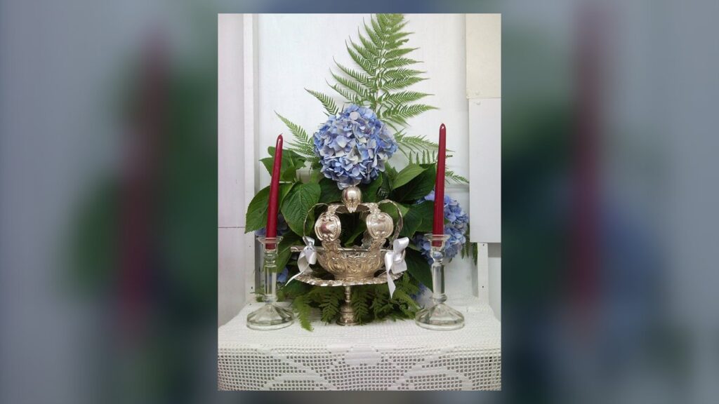 Coroa de prata do Divino entre velas e flores, usada na coroação do imperador da festa