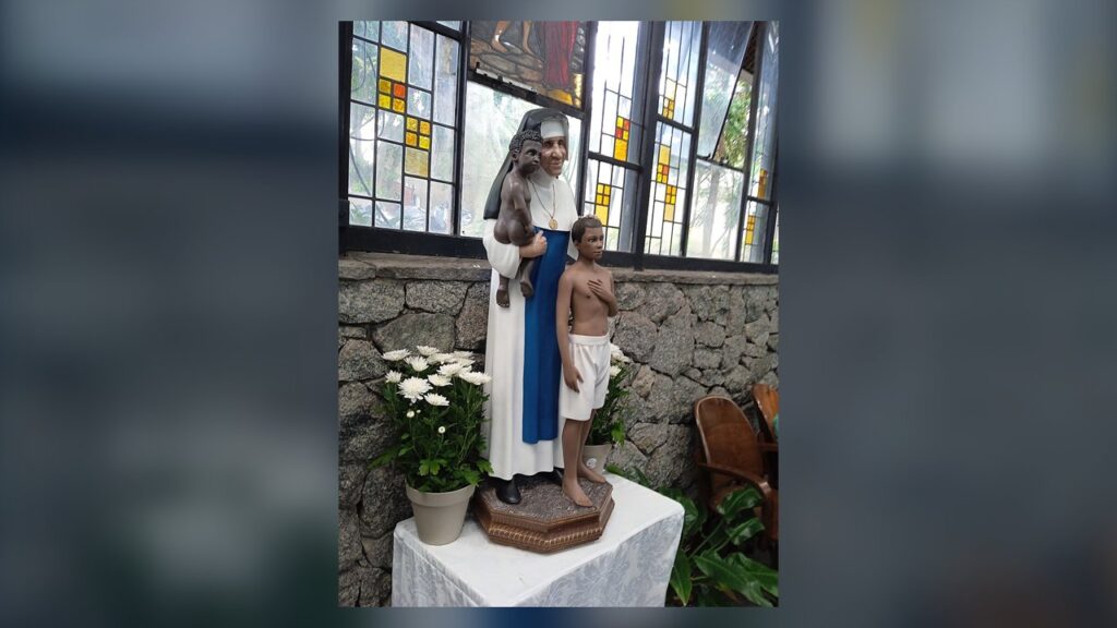 Estátua de Santa Dulce dos Pobres com o hábito azul e branco, levando ao colo uma criança pobre