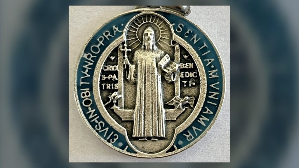 Frente da medalha de São Bento: o santo com a cruz e a Regra, o cálice e o corvo, e a oração da borda