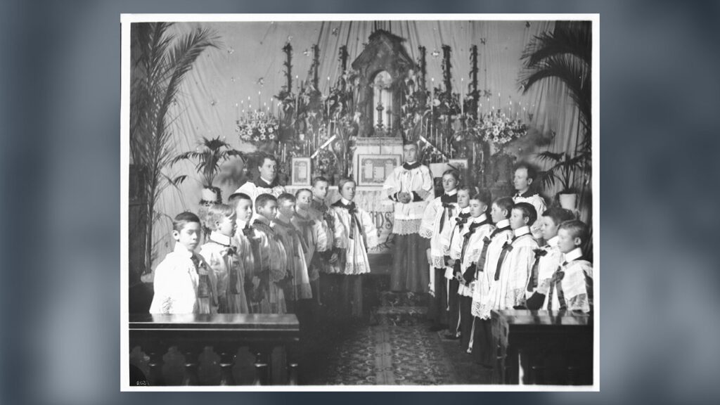 Grupo de coroinhas de sobrepeliz com os sacerdotes diante do altar de uma igreja em 1900