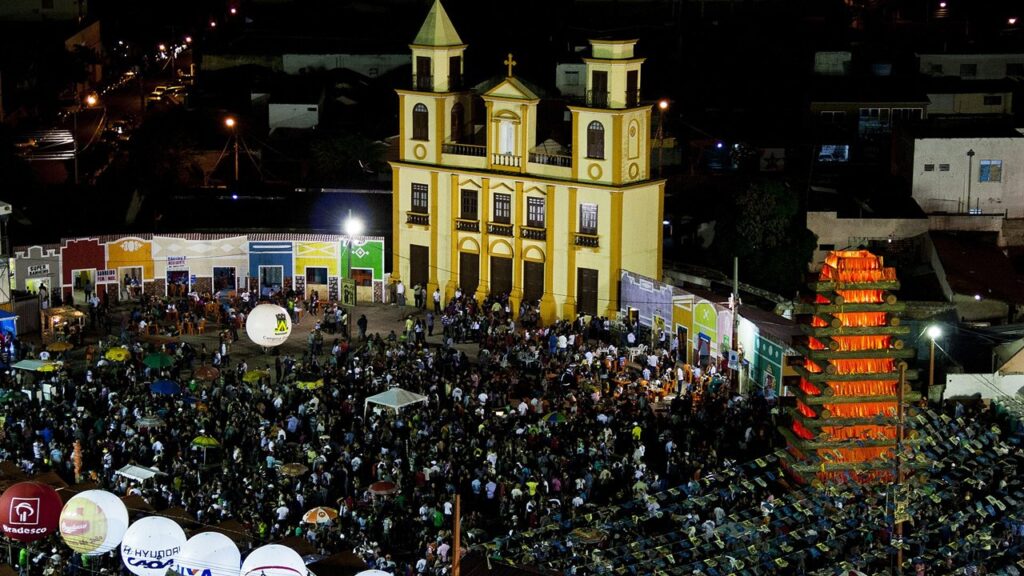 Multidão diante da capela e da fogueira cenográfica do arraial de Campina Grande, no Nordeste